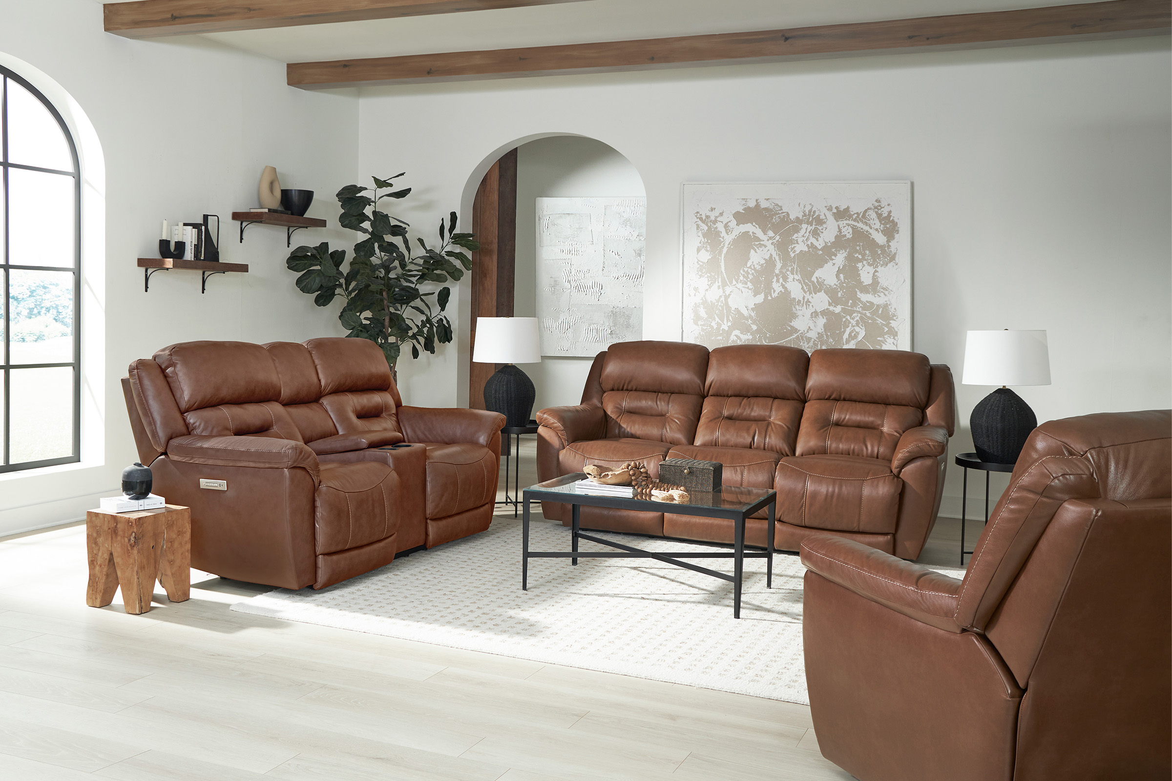 A group of matching brown leather couch, loveseat, and chair sits inside a brightly lit white living room.