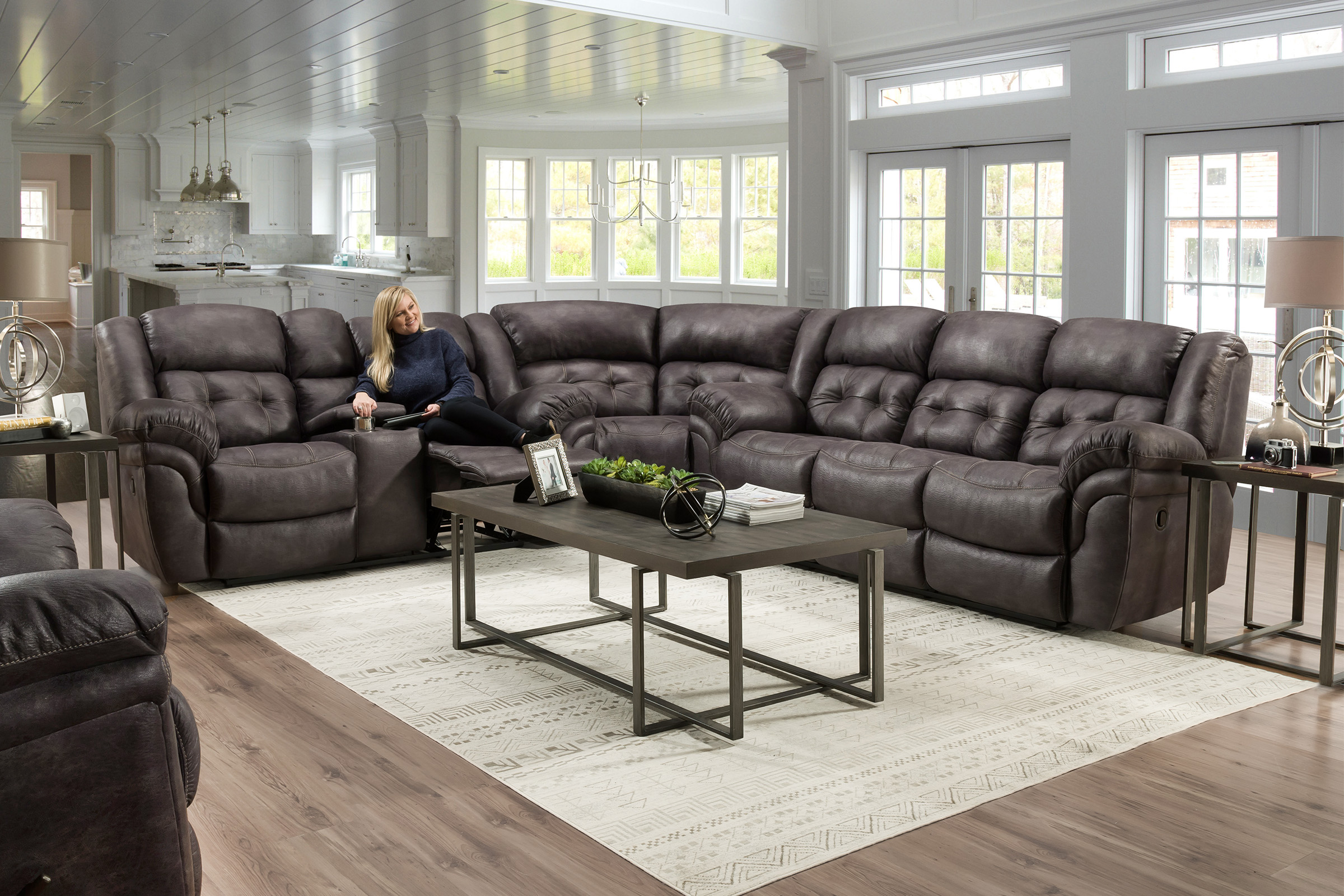 A lady sits on a tufted, dark brown leather sectional with the footrest raised.