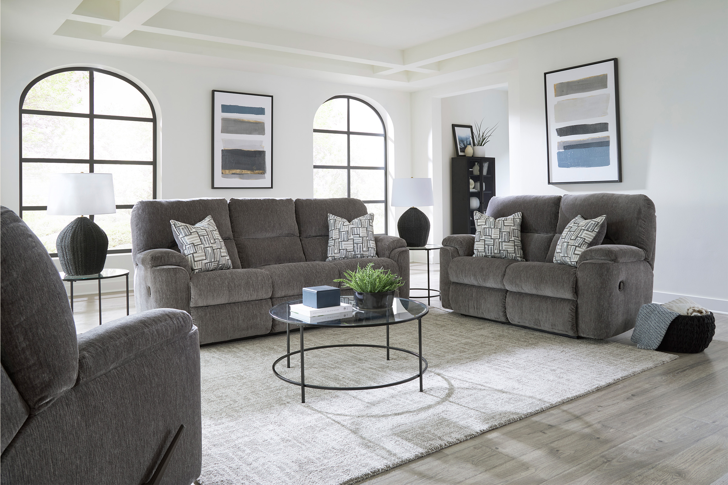 A set of cushioned, grey upholstered furniture sit in a white living room.