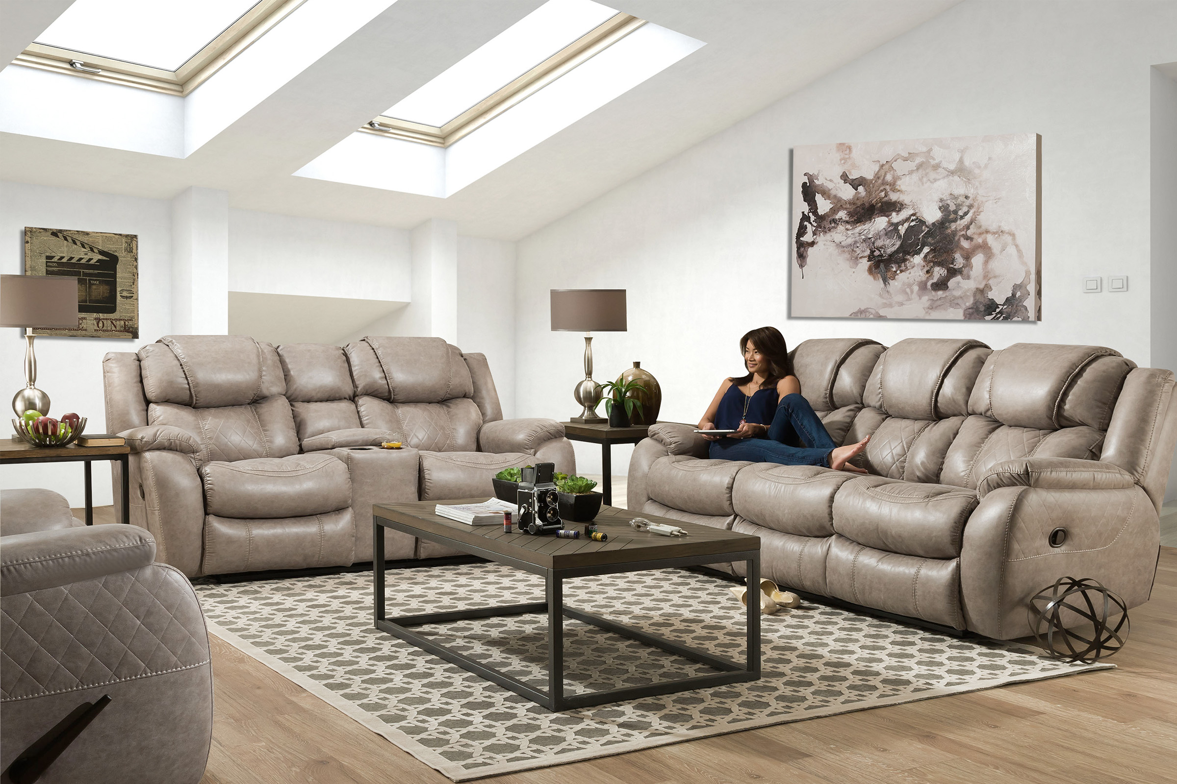 A woman sits on a well cushioned, beige leather couch. A matching loveseat and chair sit next to and across from the couch.