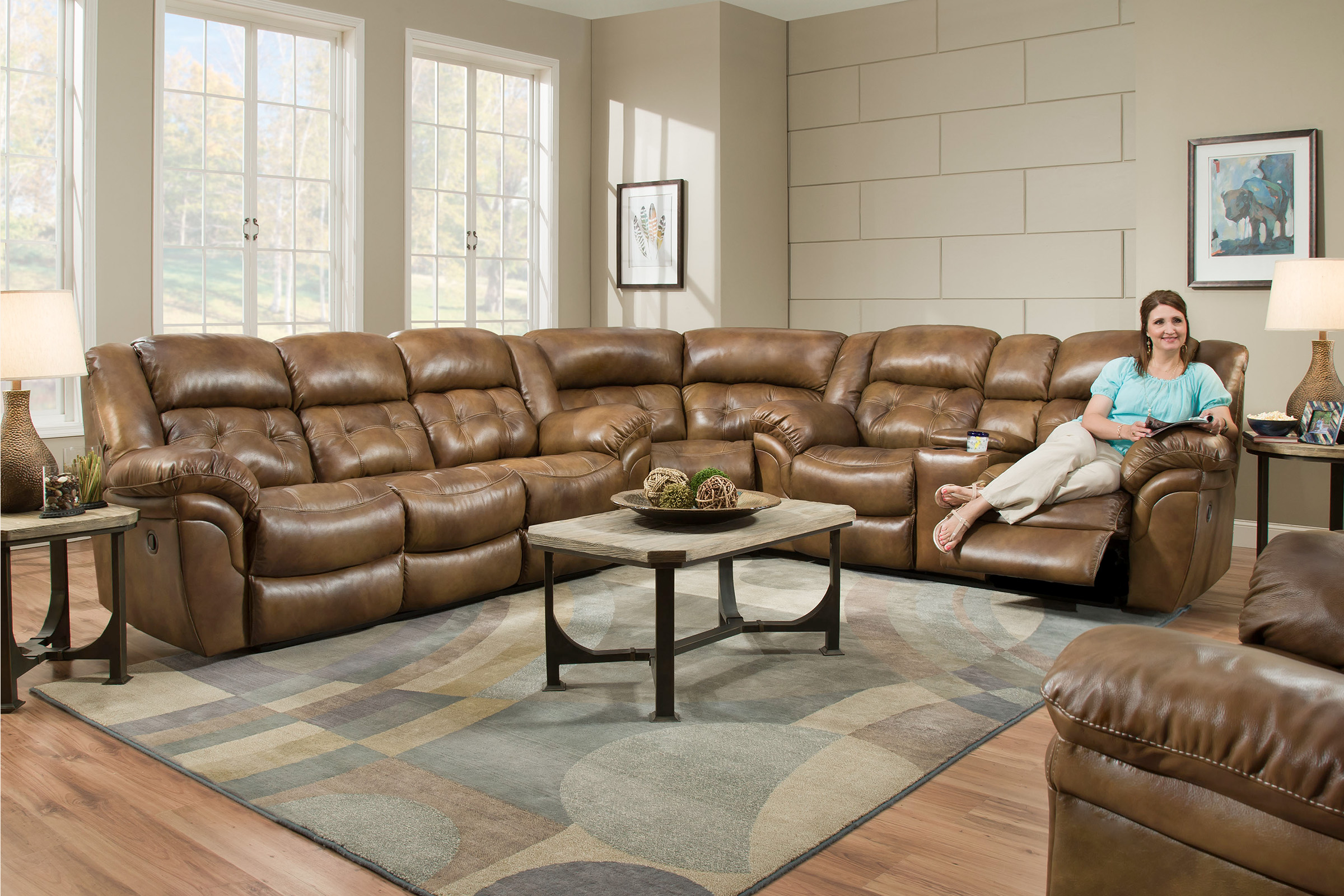 A lady sits with the footrest up in a large sectional upholstered in shiny, warm brown leather.