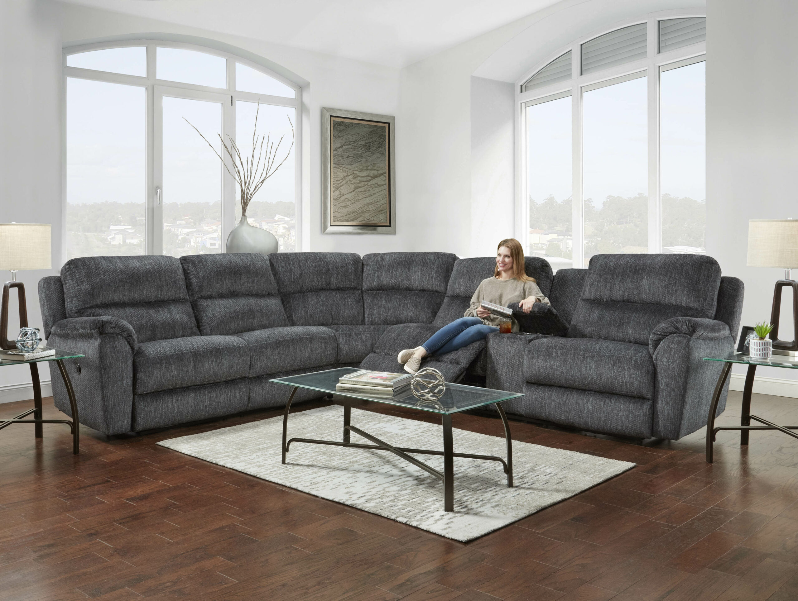 A woman sitting on a dark grey cushioned sectional displays the footrest capabilities.